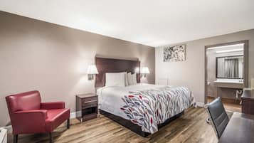 Een hotelkamer met een bed, een rode stoel, een bureau, een spiegel en een wandlamp.