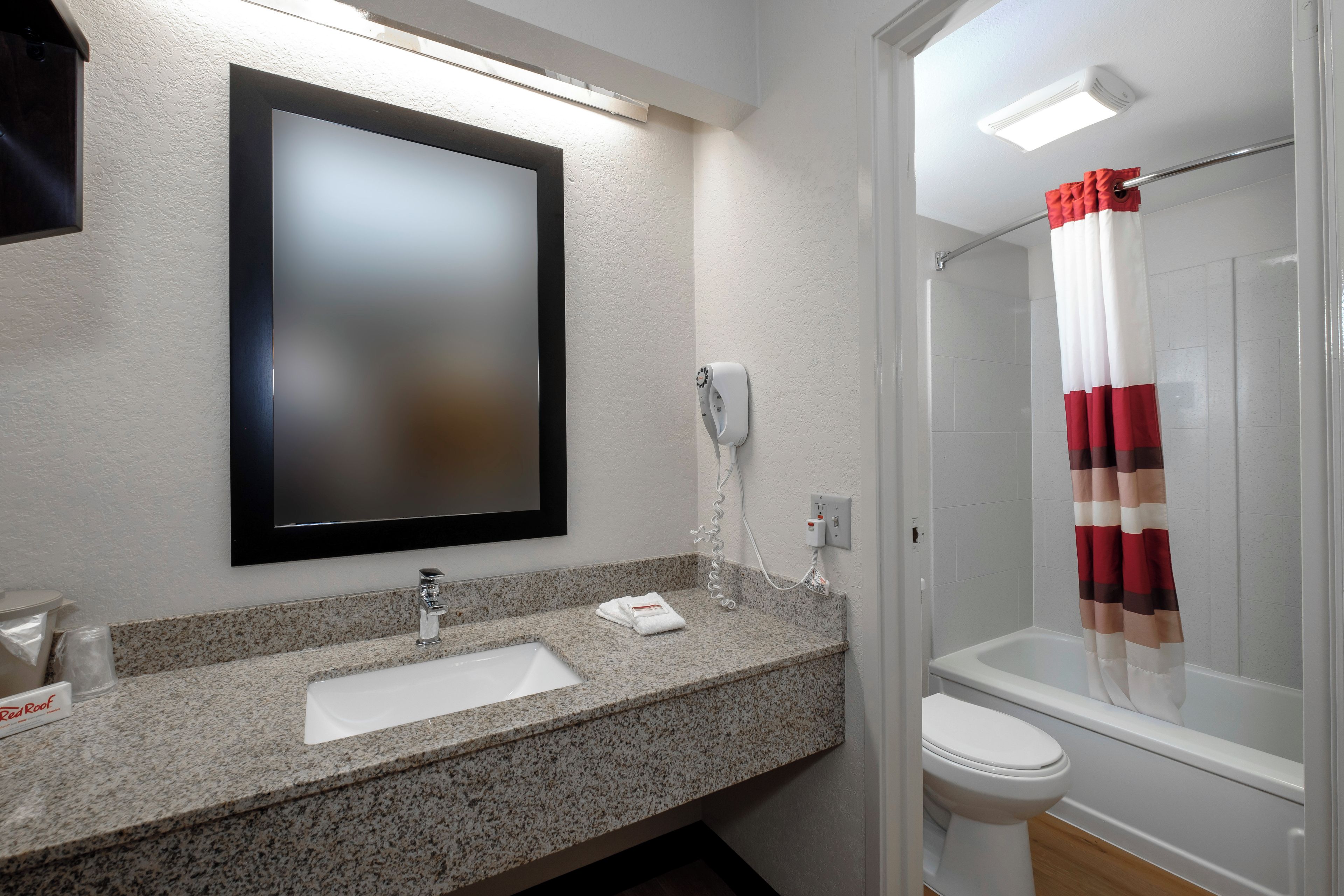 Une salle de bain avec un comptoir en granit, un lavabo blanc, un miroir, une douche avec un rideau rayé de rouge et de blanc, et des toilettes.