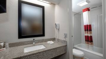 Une salle de bain avec un comptoir en granit, un lavabo blanc, un miroir, une douche avec un rideau rayé de rouge et de blanc, et des toilettes.