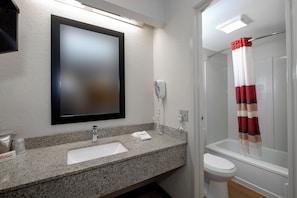 A bathroom with a granite countertop, a white sink, a mirror, a shower with a red and white striped curtain, and a toilet. - Red Roof Inn Sumter (Sumter)