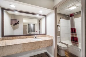 A bathroom with a granite countertop sink, a mirror, a toilet, and a shower with a striped curtain. - Red Roof Inn Sumter (Sumter)