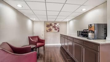 Een hotel lobby met een zithoek, een koffiehoek en een muur met een kunstwerk van een palmboom.