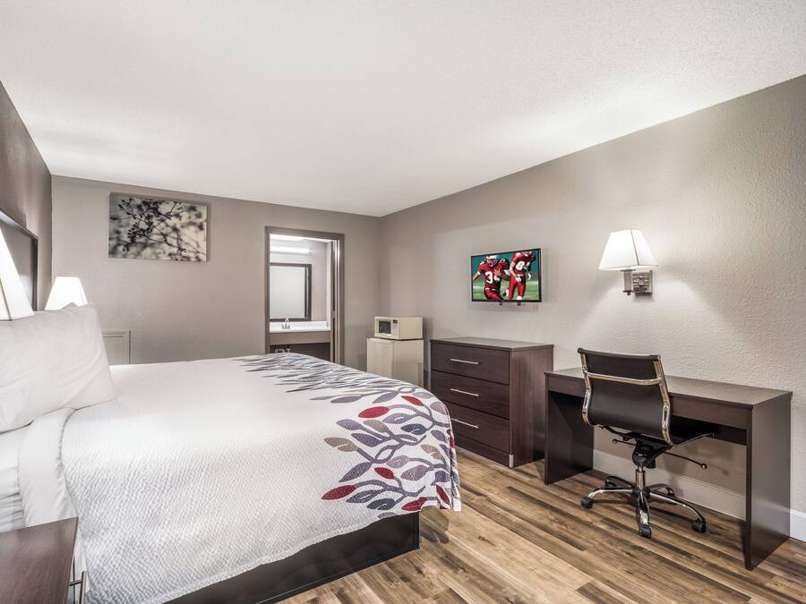 A hotel room with a bed, a desk, a chair, a television, and a microwave.