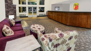 A lobby with a red sofa, patterned armchairs, a small table, and a reception desk. - Super 8 by Wyndham Central Pt Medford (Central Point)