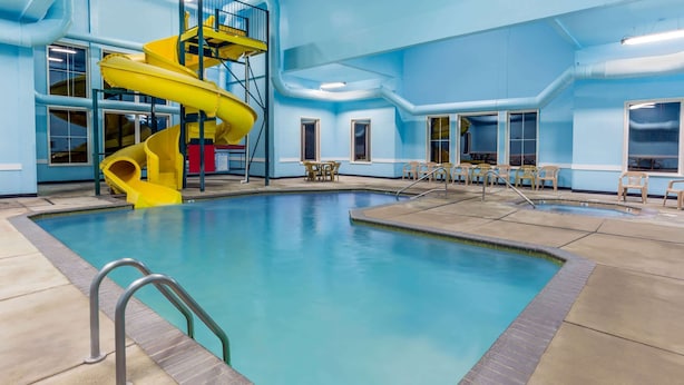 An indoor swimming pool with a yellow spiral slide, clear blue water, and a tiled floor. - Super 8 by Wyndham Central Pt Medford (Central Point)