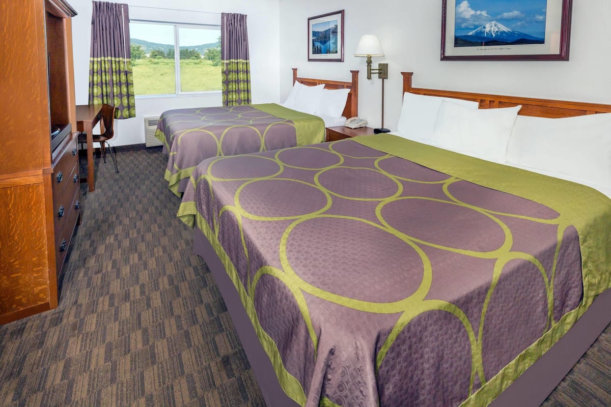 A hotel room with two beds, a desk, a chair, a lamp, and a window with curtains.