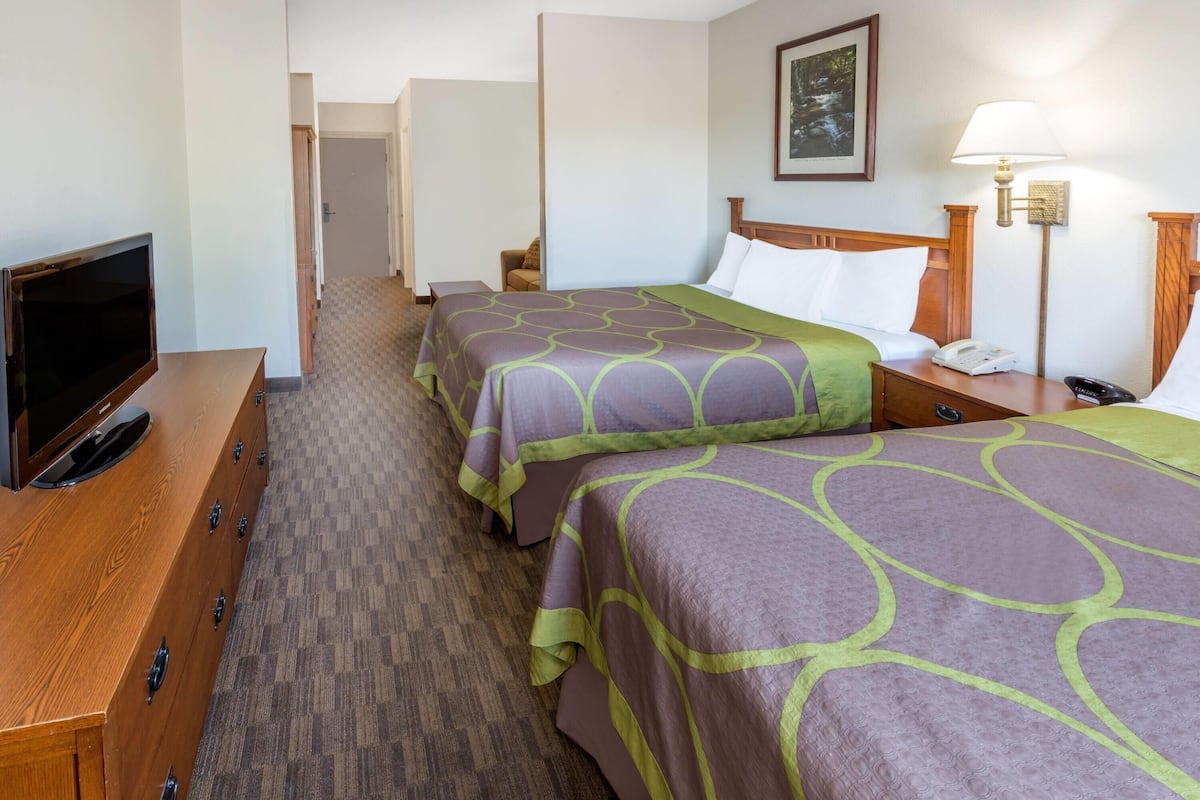 A hotel room with two beds, a TV, a desk, and a lamp.