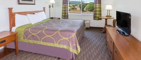Quarto de hotel com cama, televisão, escrivaninha, cadeira, luminária, janela com cortinas e quadro na parede.