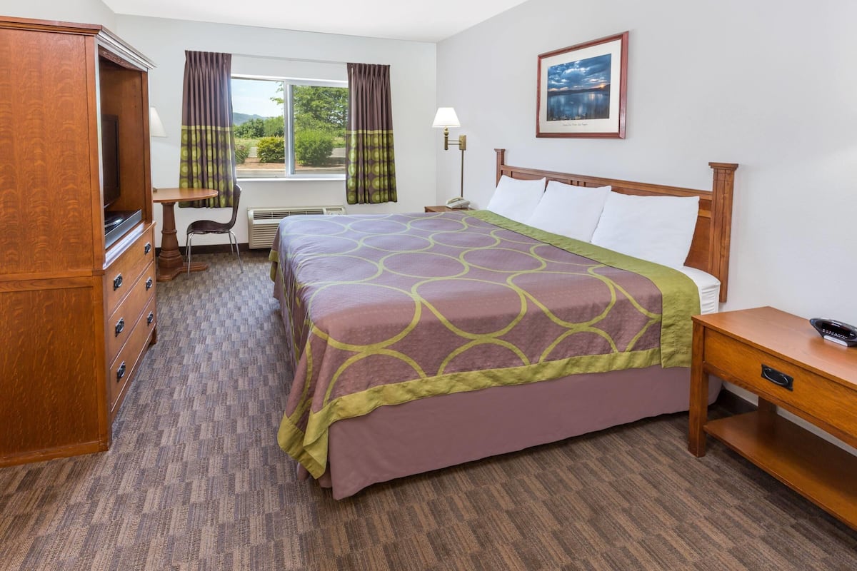 A hotel room with a bed, a desk, a chair, a TV, a lamp, and a window with curtains.