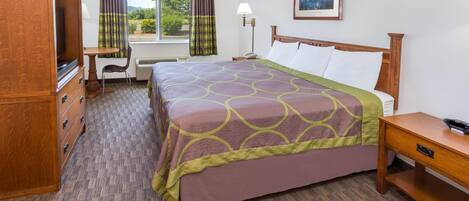 Habitación de hotel con cama, escritorio, silla, televisor, lámpara y ventana con cortinas.
