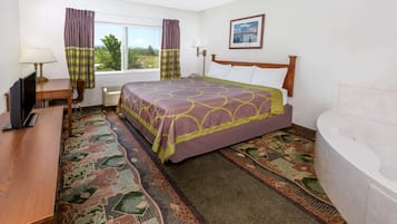 Habitación de hotel con cama, escritorio con computadora, silla, ventana con cortinas, lámpara de pared, cuadro enmarcado y bañera.