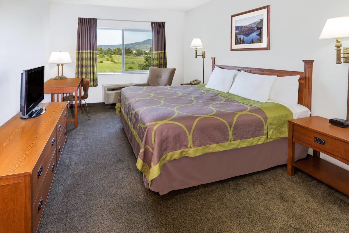 A hotel room with a bed, a desk with a TV, a chair, and a window with curtains.