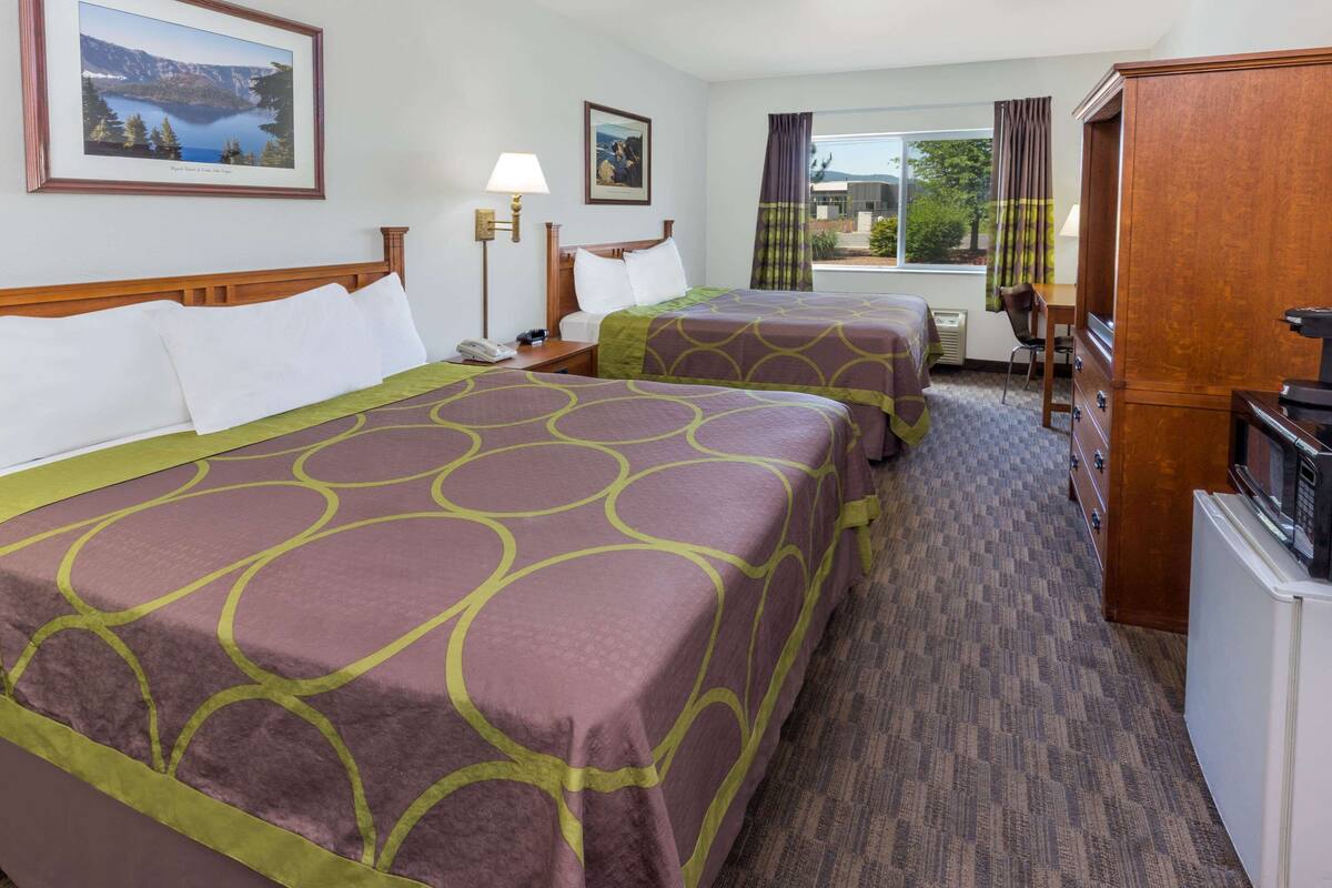 A hotel room with two beds, a desk, a chair, a refrigerator, and a window with curtains.
