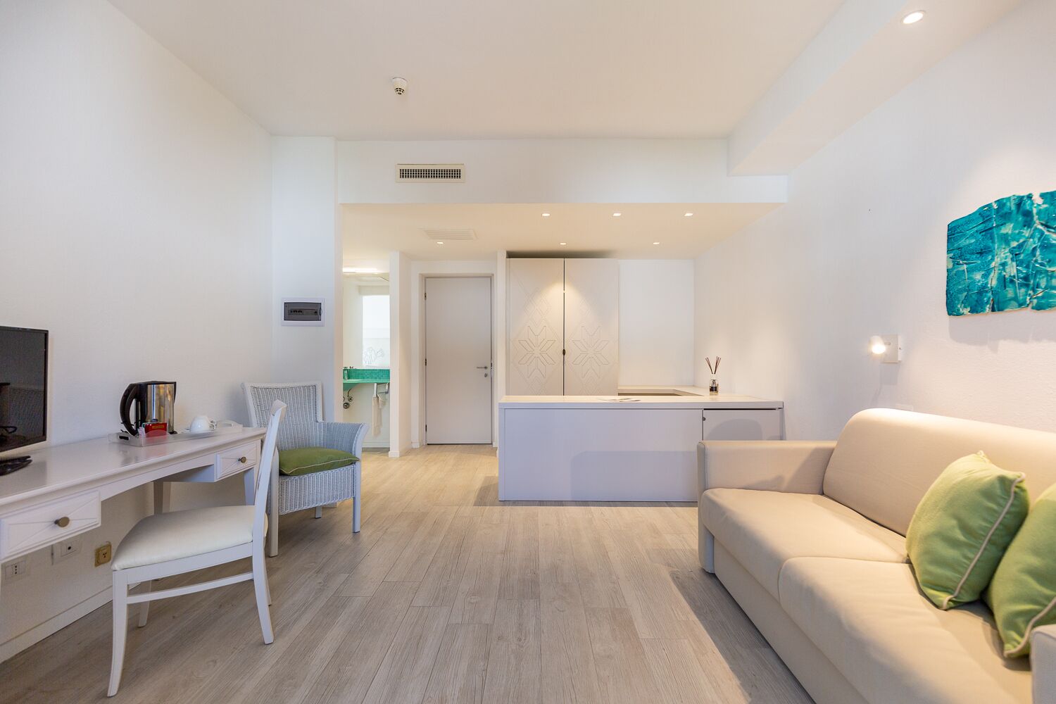 A modern living room with a white sofa, a dining area with a white table and chairs, and a kitchen area with a white countertop and cabinets.