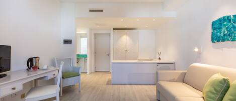 A modern living room with a white sofa, a dining area with a white table and chairs, and a kitchen area with a white countertop and cabinets.