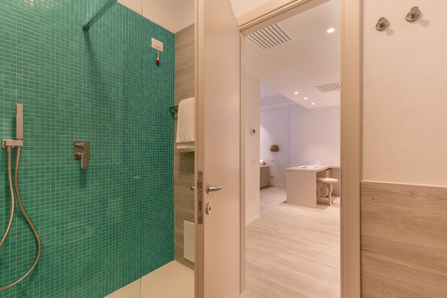 A modern bathroom with a green tiled shower wall, a white towel, and a wooden floor.