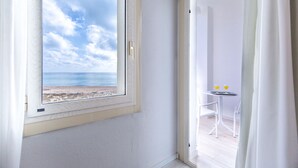 Een kamer met uitzicht op een strand en zee, een tafeltje met twee glazen, en een witte stoel.