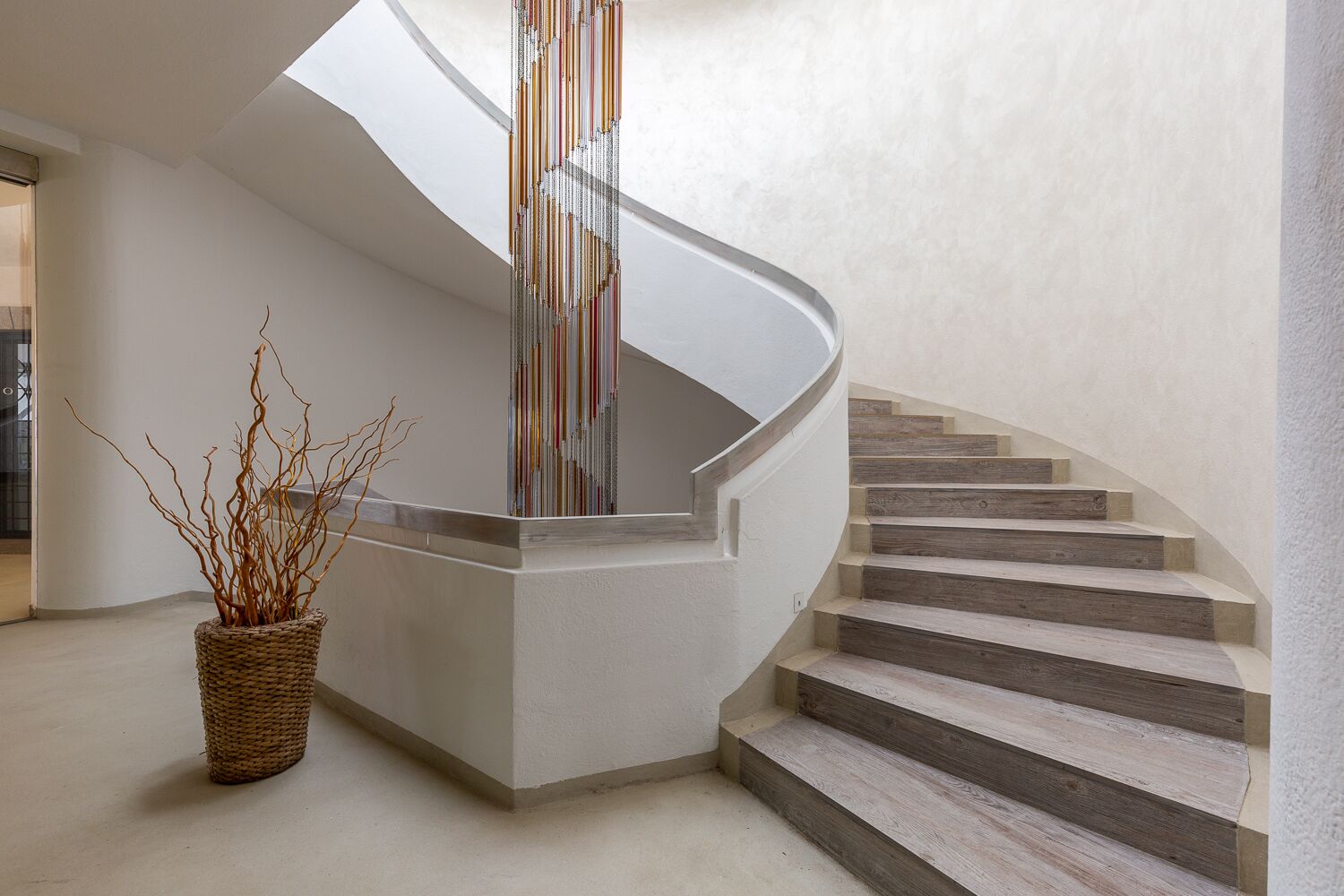 A modern spiral staircase with a minimalist design, a woven basket with branches, and a textured wall.