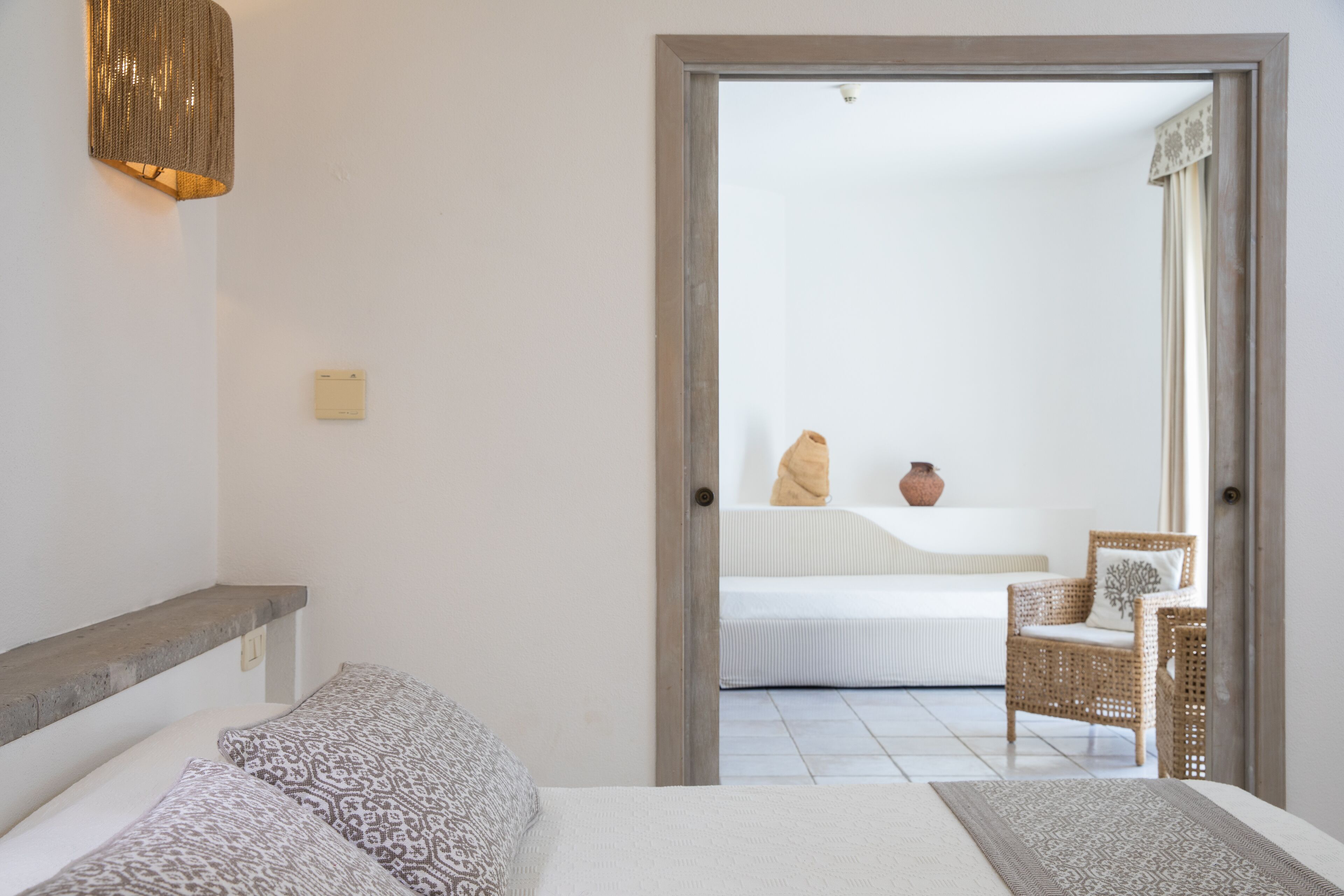 Un dormitorio con una cama, una mesita de noche, una silla y vistas a otra habitación con una cama y un florero.