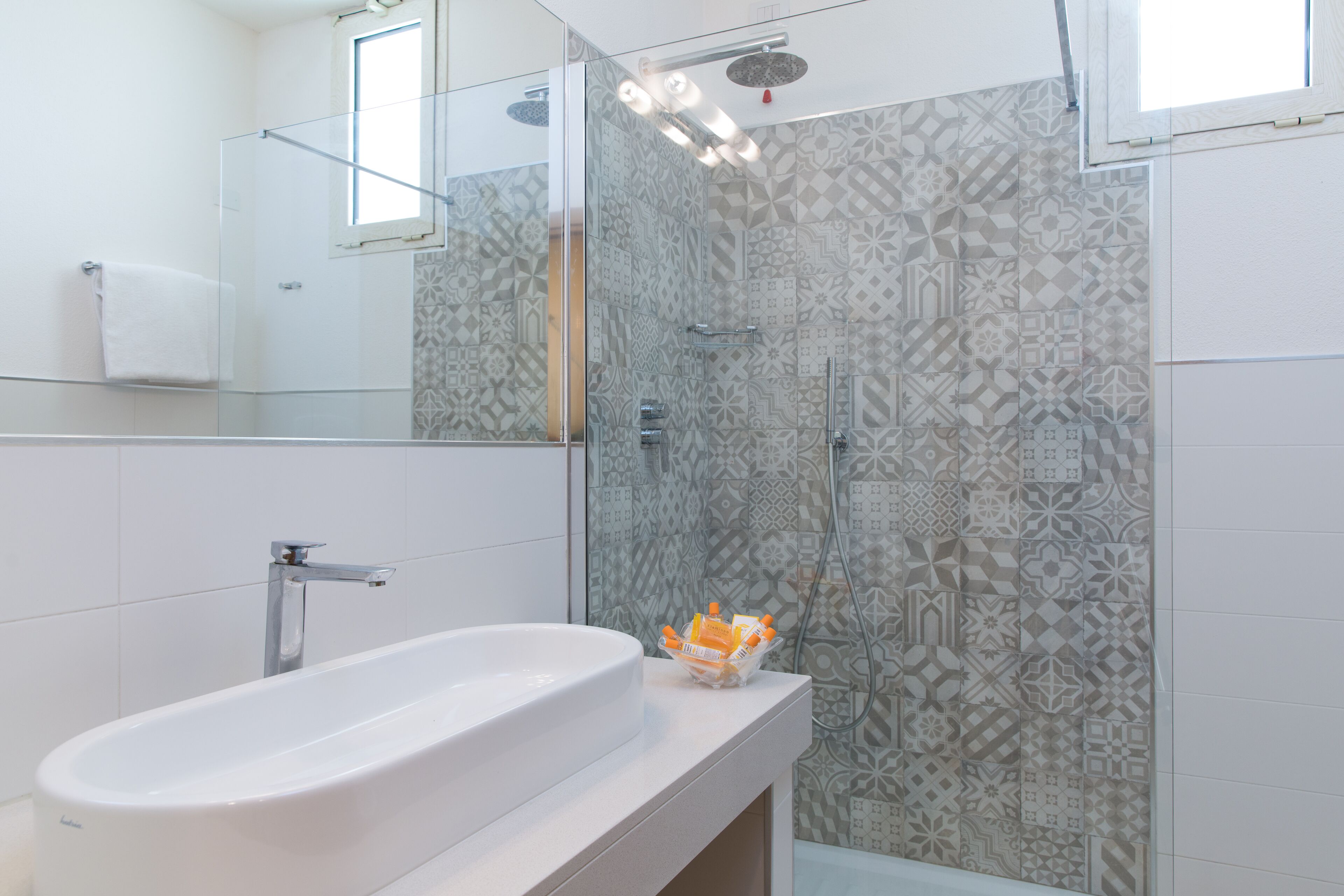 A modern bathroom with a white sink, a glass shower enclosure, and patterned tiles.