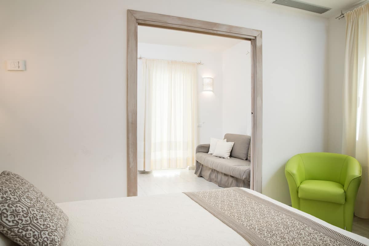 A bedroom with a bed, a green chair, a sofa, and a patterned rug.