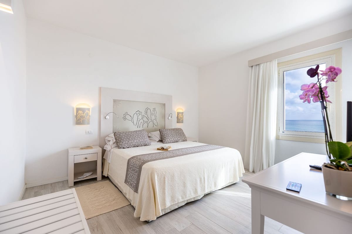 A modern bedroom with a bed, bedside tables, a desk, and a window with curtains.