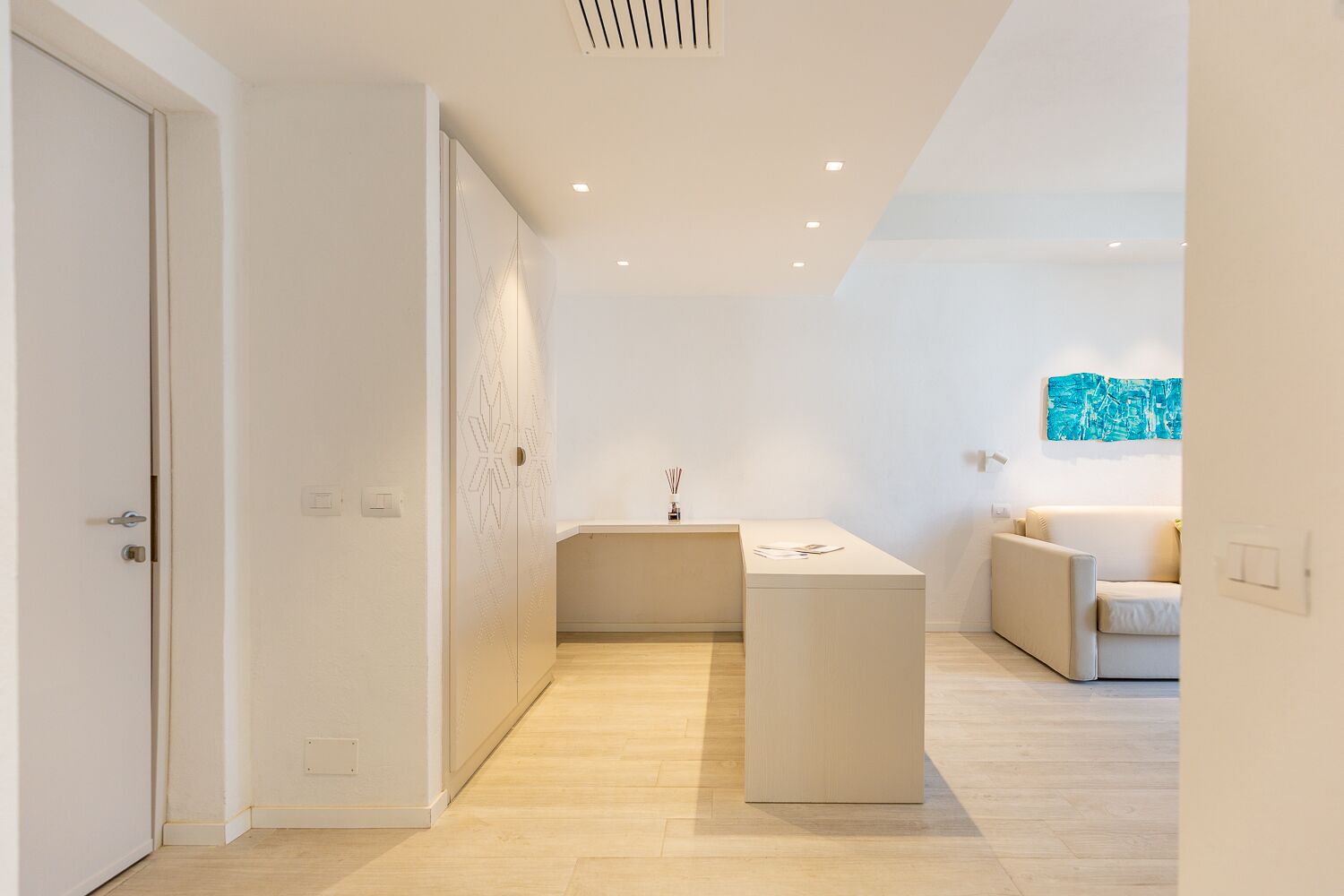Ein modernes, minimalistisches Hotelzimmer mit Holzboden, einer zentralen Insellösung mit Waschbecken, einer Couch und einem Wandbild im abstrakten Stil.