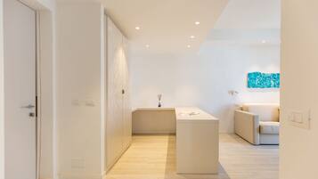 Ein modernes, minimalistisches Hotelzimmer mit Holzboden, einer zentralen Insellösung mit Waschbecken, einer Couch und einem Wandbild im abstrakten Stil.