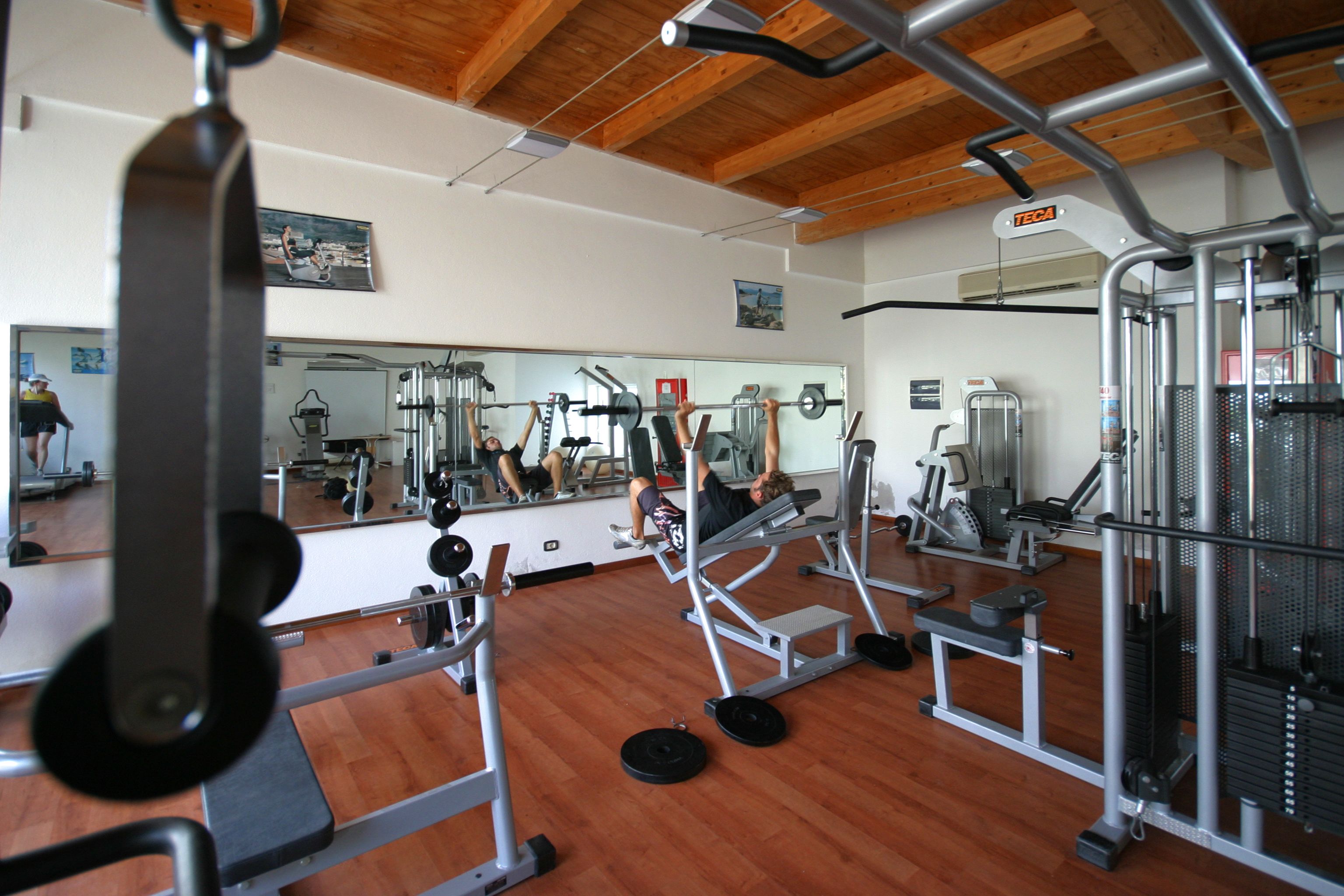Un gimnasio con diverso equipo de ejercicio, un espejo grande y suelo de madera.