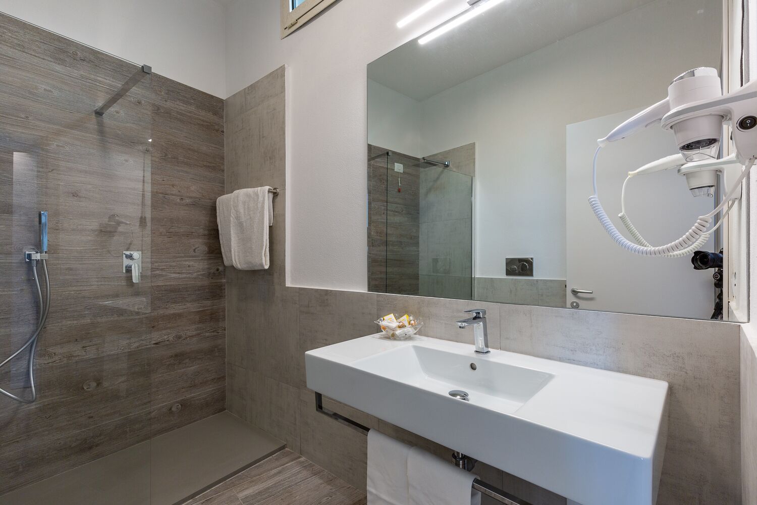 A modern bathroom with a walk-in shower, a large mirror, and a white sink.