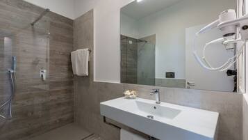 A modern bathroom with a walk-in shower, a large mirror, and a white sink.