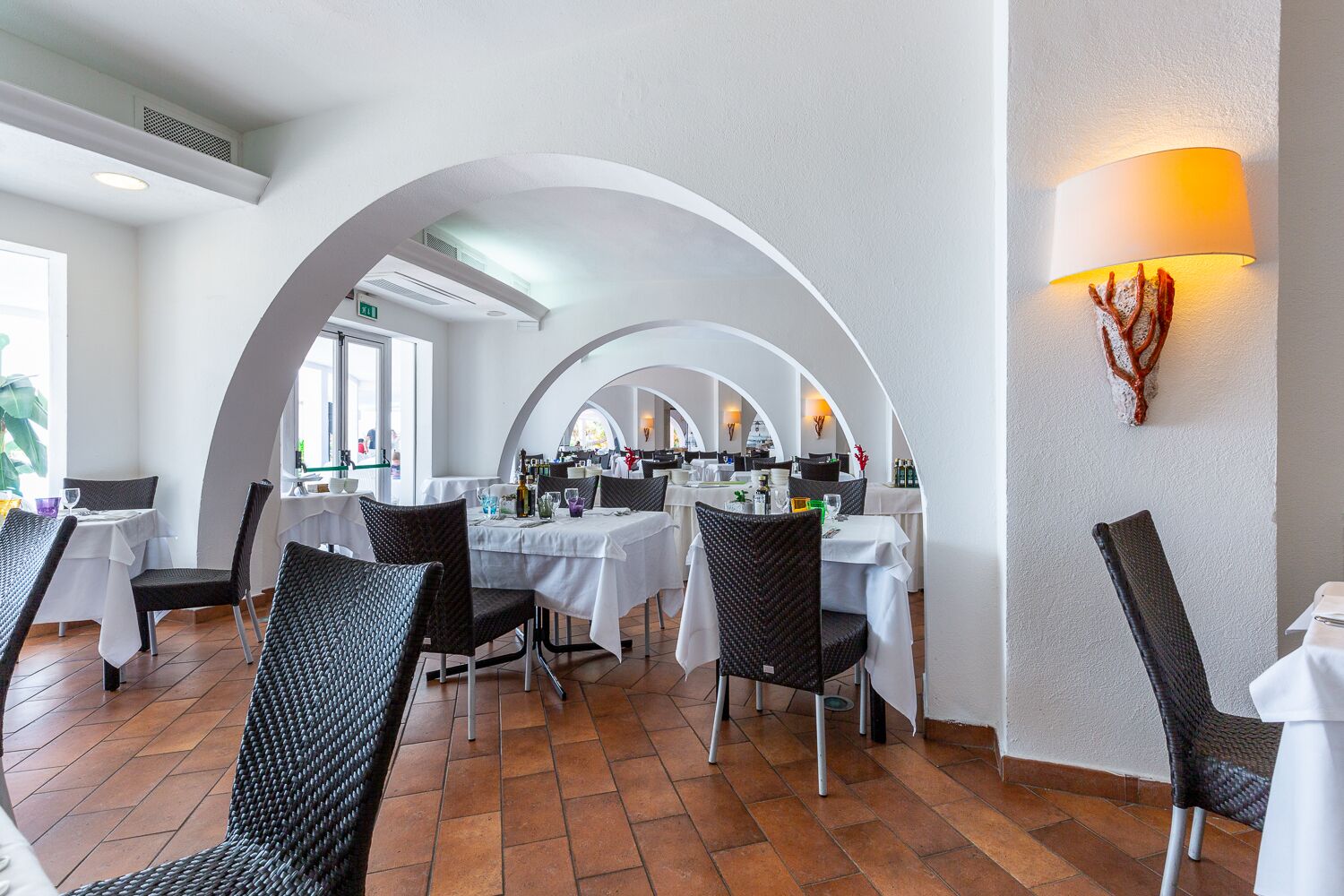 Un restaurant avec des tables et des chaises blanches, des plafonds en arc de cercle et une lampe fixée au mur.