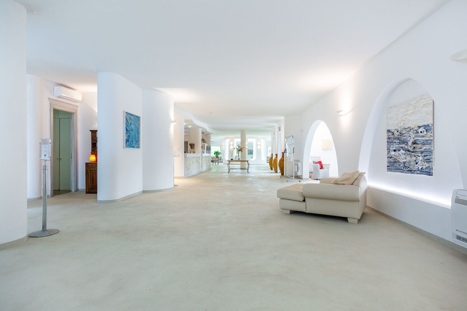 Un pasillo amplio con un sofá beige, paredes blancas y obras de arte.