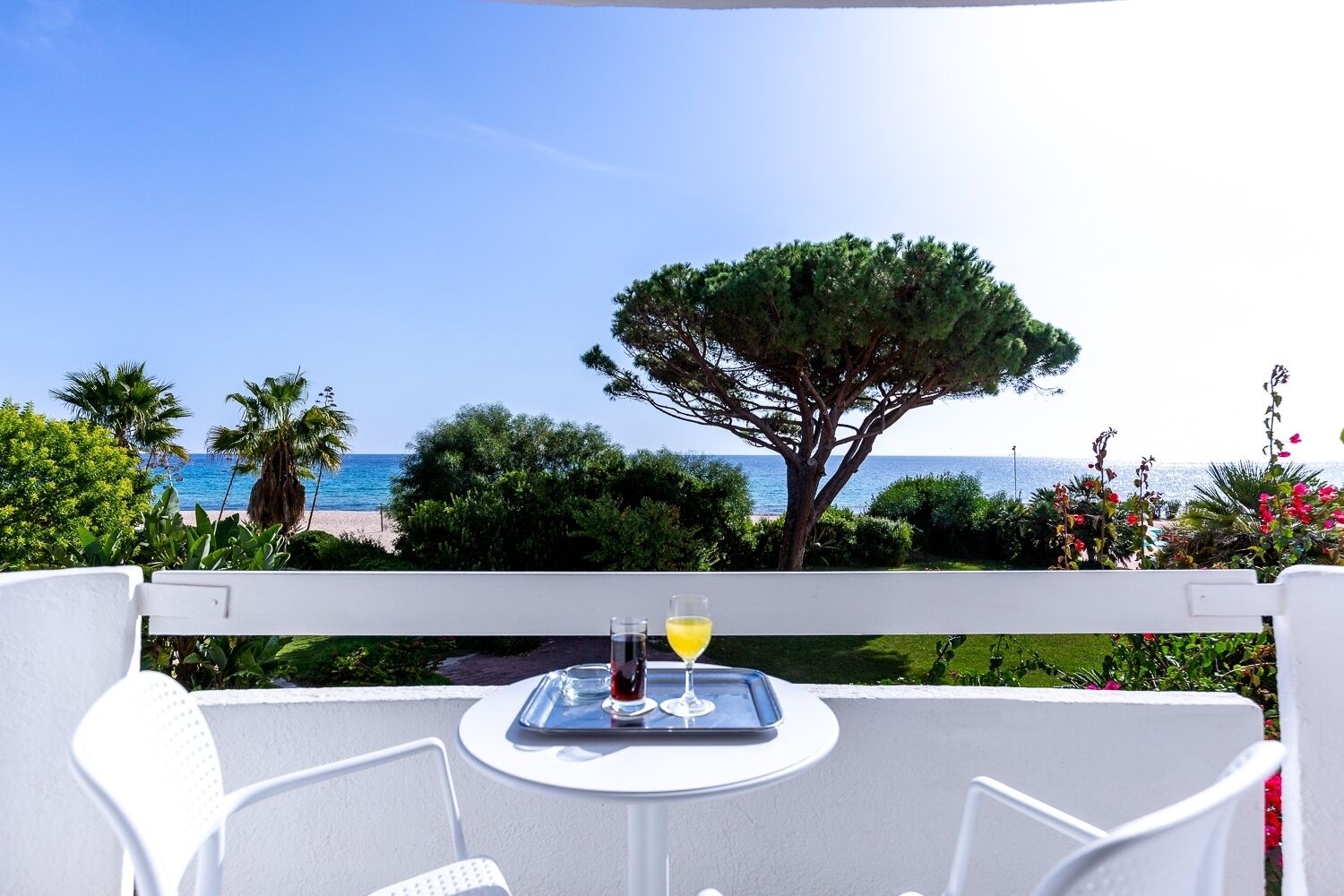 A balcony with a table set for two, overlooking a beach and the sea.