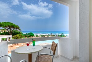 Een balkon met een tafel en stoelen, met uitzicht op een strand en zwembad.