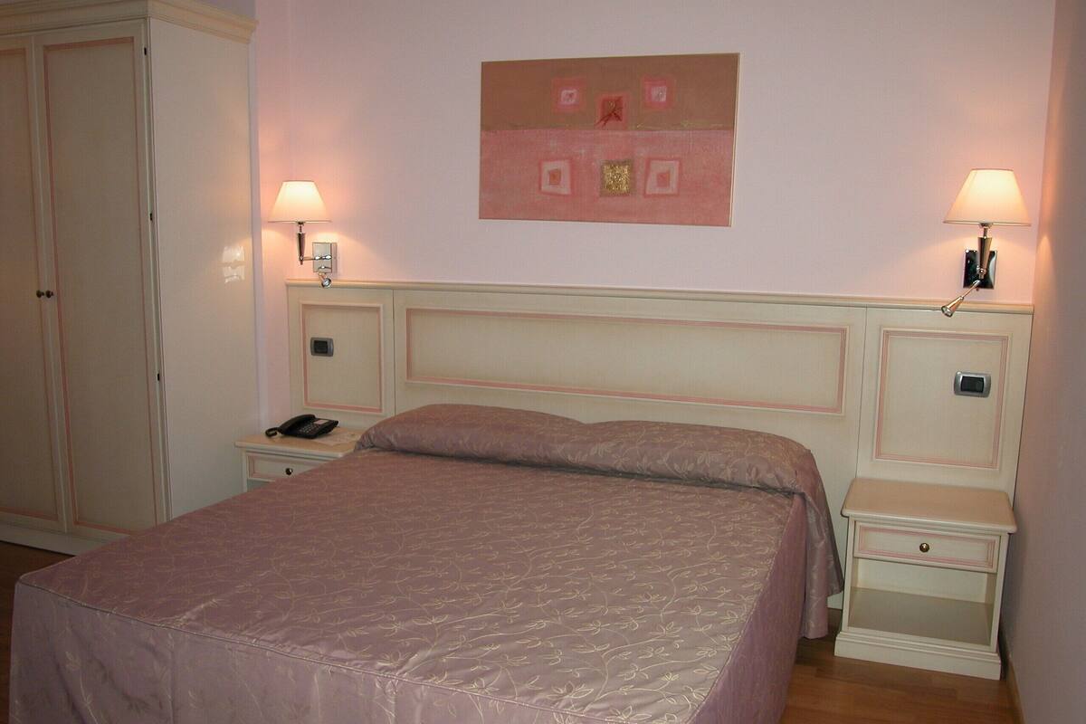 A bedroom with a large bed, two bedside tables, a nightstand, a wardrobe, and a wall clock.
