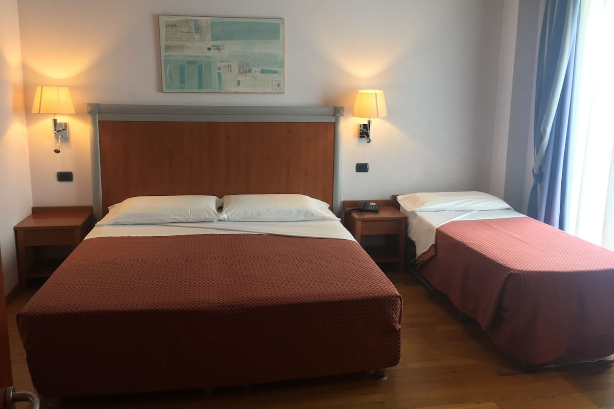 A hotel room with two beds, a wooden headboard, two bedside tables with lamps, and a painting on the wall.