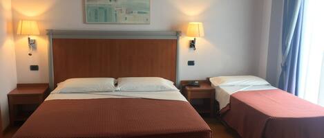 Una habitación de hotel con dos camas, cabecero de madera, dos mesitas de noche con lámparas y un cuadro en la pared.