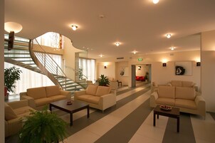A spacious lobby with a central staircase, multiple seating areas, and a large plant.