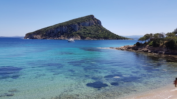 On distingue clairement une zone côtière avec une île rocheuse imposante et un bateau sur l’eau.