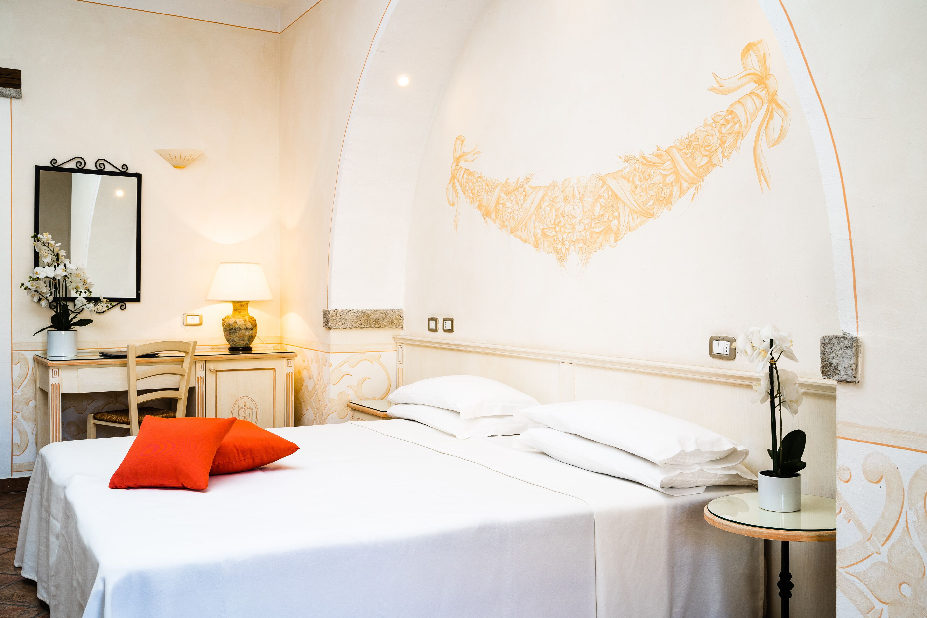 Ein Hotelzimmer mit einem Bett, einem Schreibtisch und einem Stuhl. Auf dem Schreibtisch steht eine Lampe und eine Vase mit Blumen.