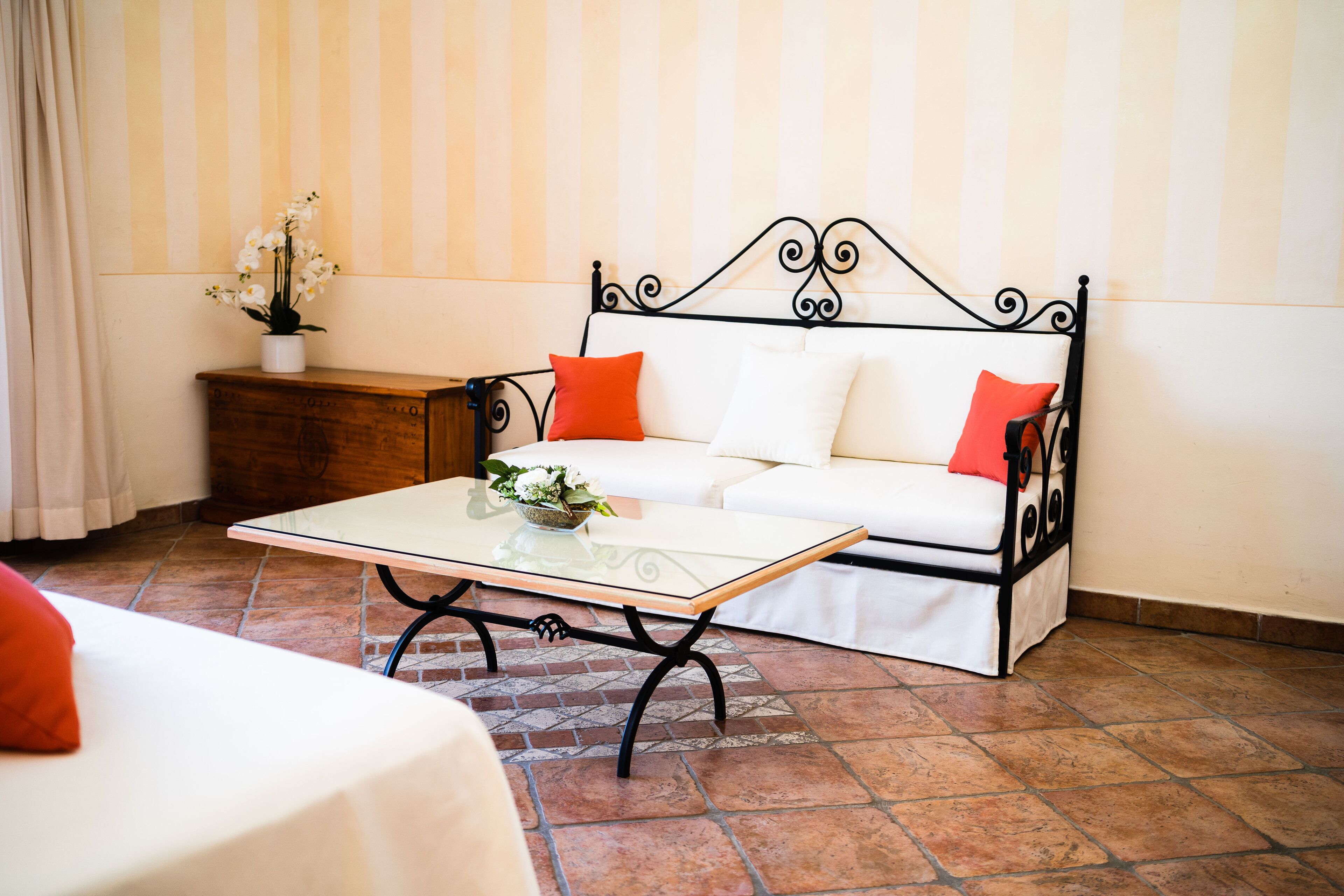Una habitación con un sofá blanco, una mesa de centro de vidrio, una mesita de noche de madera y una planta en maceta.
