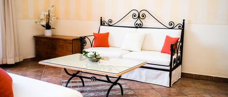 Una habitación con un sofá blanco, una mesa de centro de vidrio, una mesita de noche de madera y una planta en maceta.