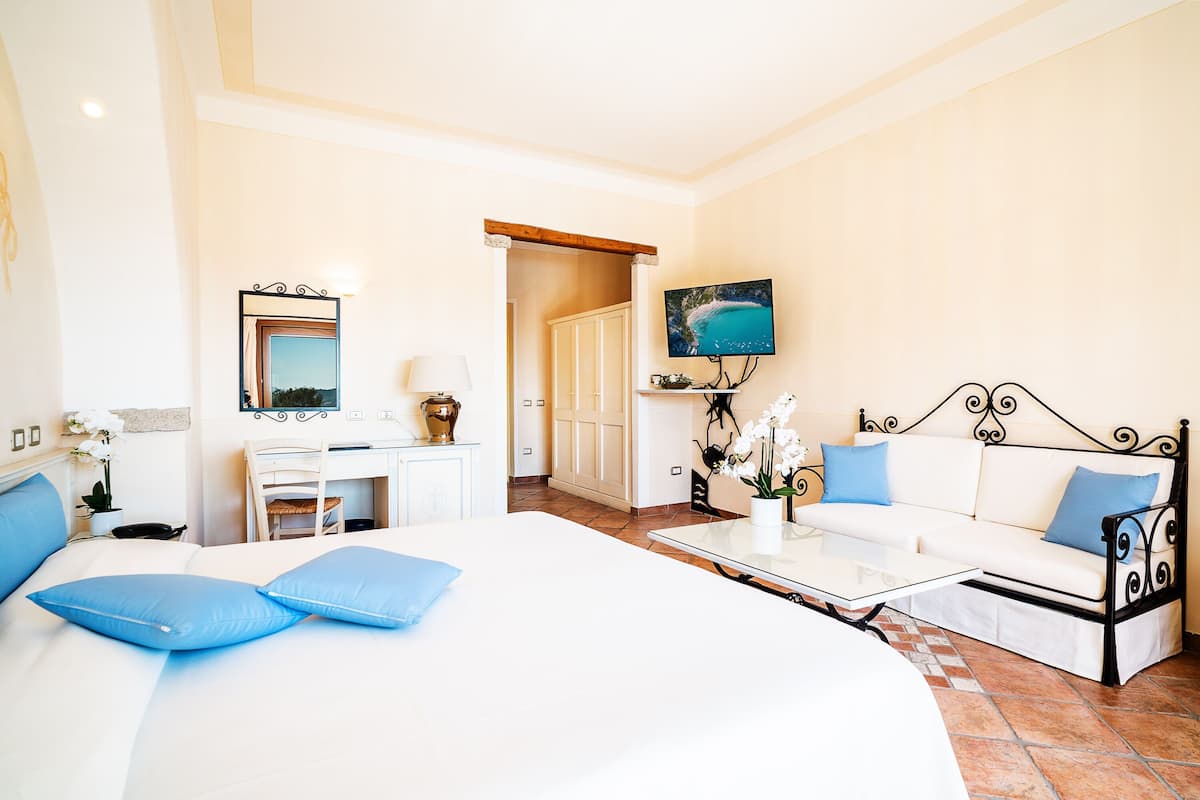 A hotel room with a large bed, a sofa, a desk, and a TV.
