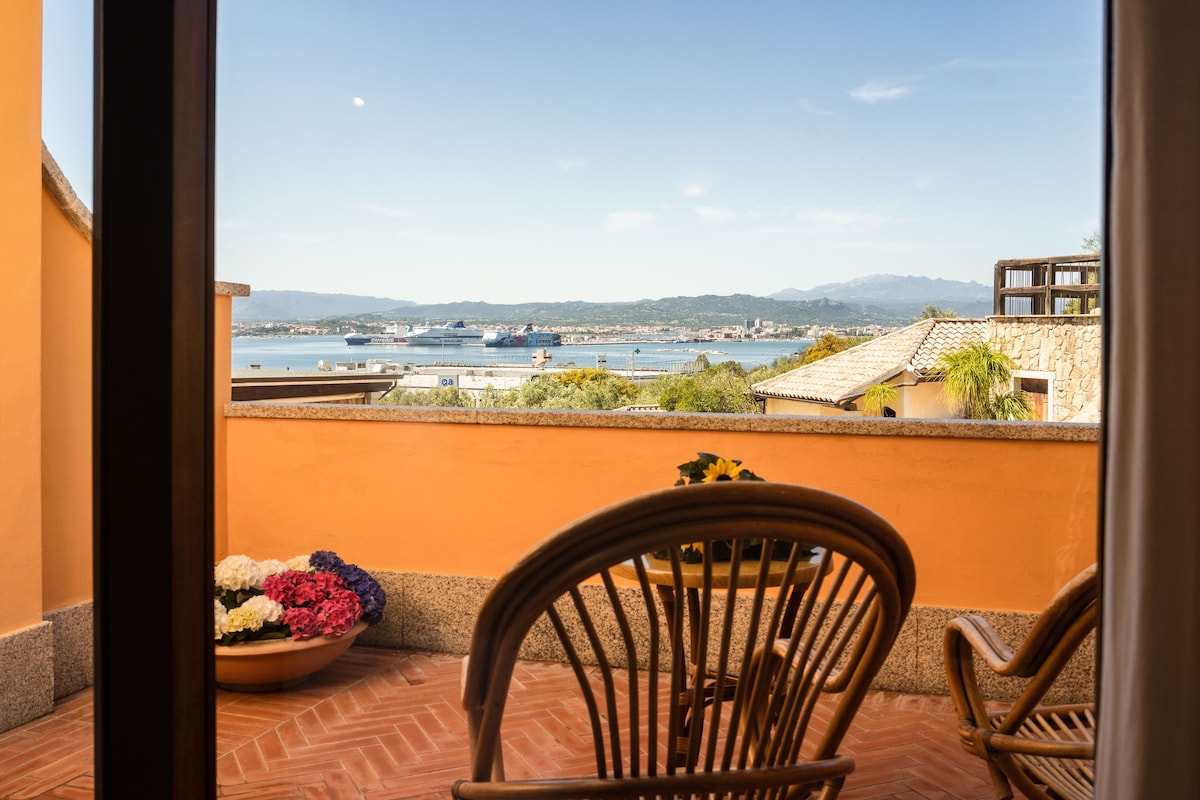 Un balcon avec vue sur la mer, un bateau et des montagnes lointaines.