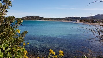 Ένα παράκτιο τοπίο με κρυστάλλινα, γαλάζια νερά, μια αμμώδη παραλία και ένα λόφωμα στο βάθος.