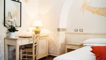 Habitación de hotel con escritorio, silla, lámpara, cama y una pared con diseño floral.