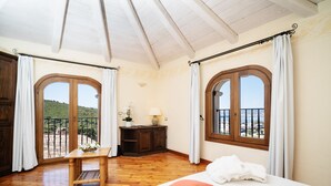 Une chambre avec un plancher en bois, un lit avec des oreillers blancs et orange, une table de chevet avec une lampe, et deux fenêtres avec des rideaux.