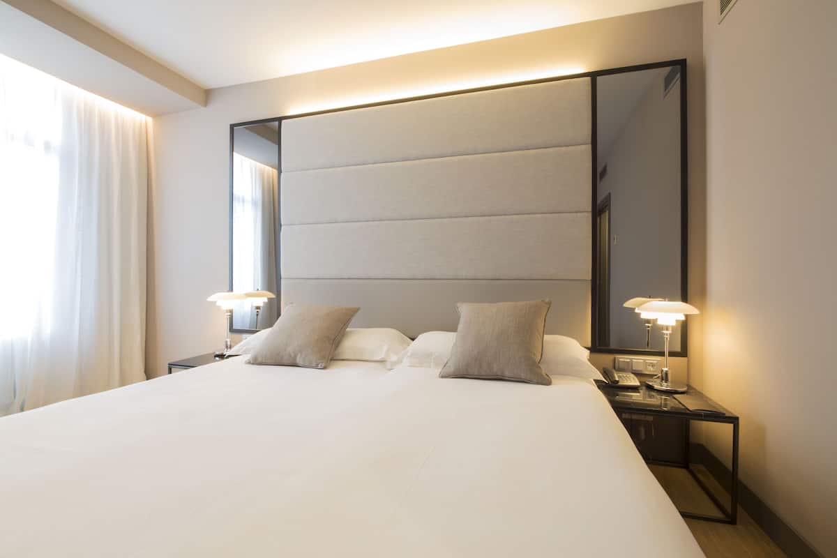 A hotel room with a large bed, two bedside lamps, a nightstand, and a large mirror.