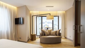 Una habitación de hotel moderna con una cama grande, un área de descanso circular, un televisor de pantalla plana y vistas a un balcón con barandilla.